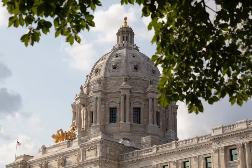 View of Minnesota state capitol dome from side with leafy tree branches slightly obscuring view.